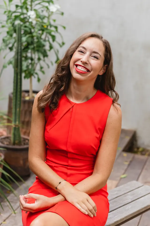 Lane Lowe, smiling and seated outdoors in a red dress.